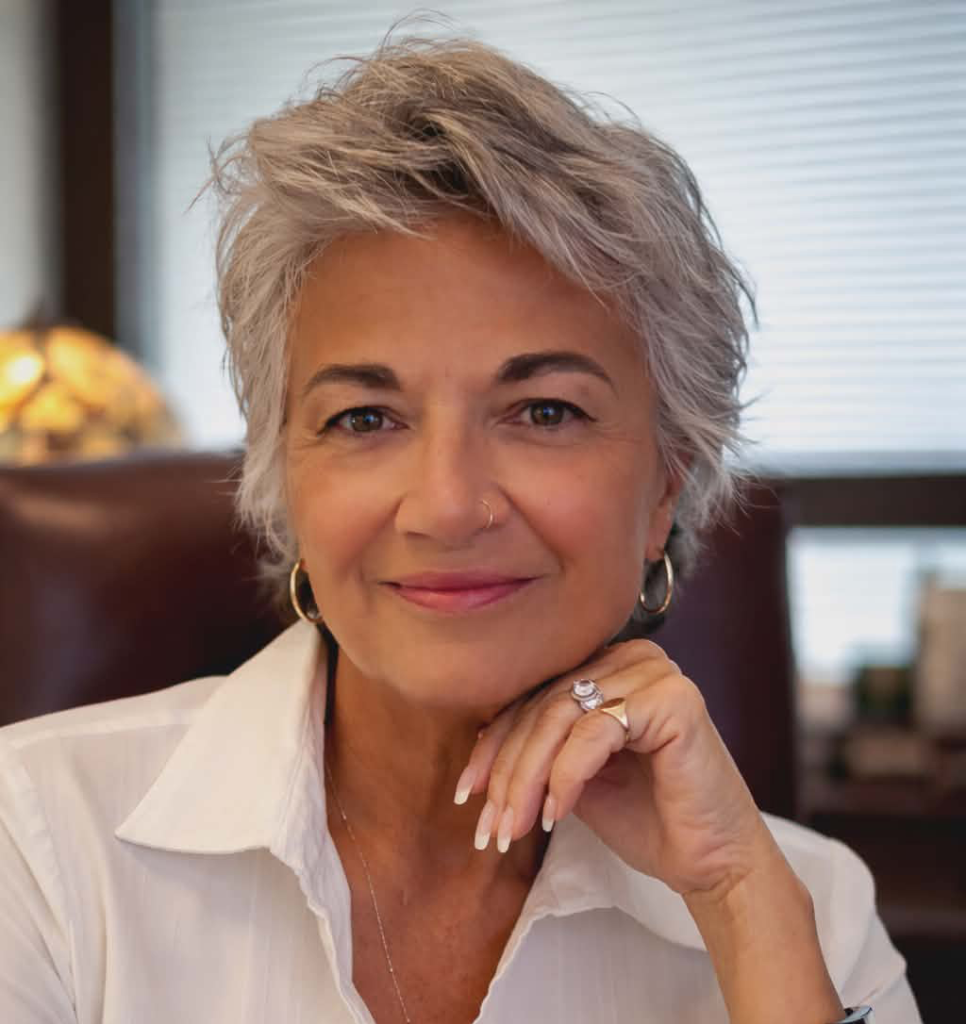 Smiling mature woman with short gray hair, wearing a white blouse and hoops.