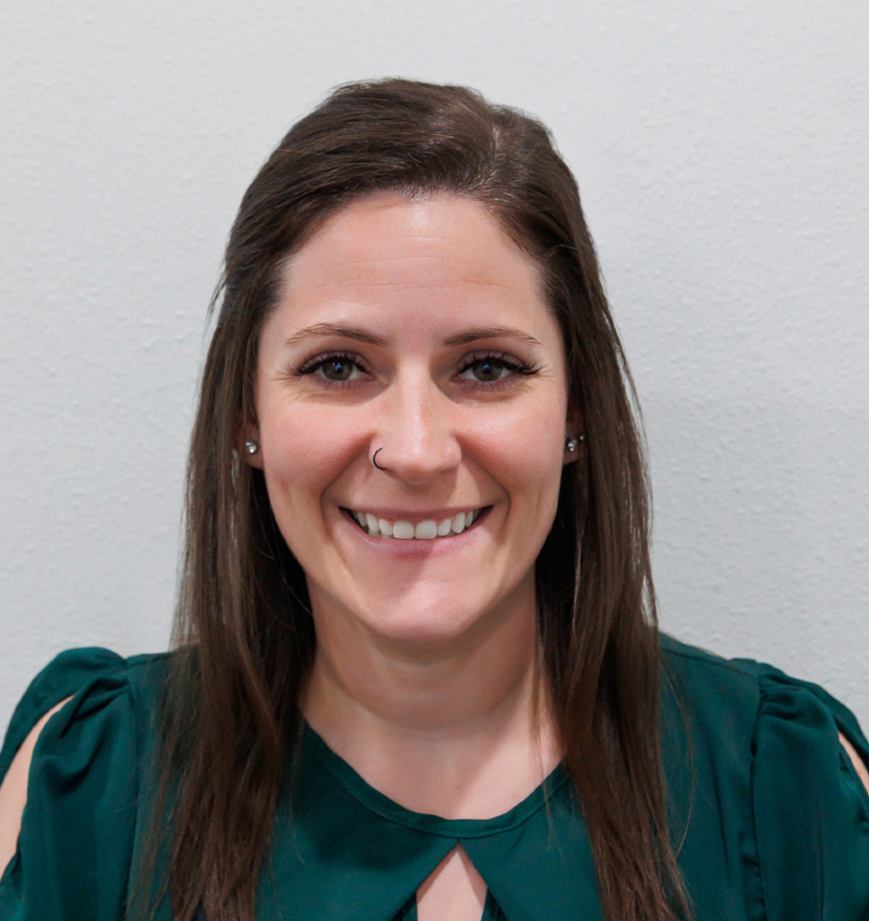 Smiling woman with long brown hair wearing a dark green top, light gray background