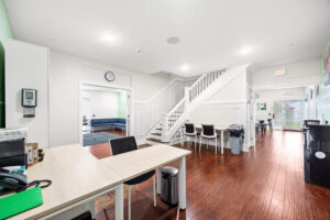Bright reception area with white walls, wood floors, staircase, desks, and seating.