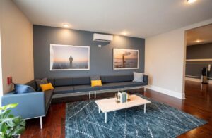 Modern living room with long blue sectional, blue accent wall, framed ocean photos, coffee table, rug.