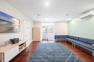 Modern waiting room with long gray sectional, TV, teak floor, and mint-green wall.
